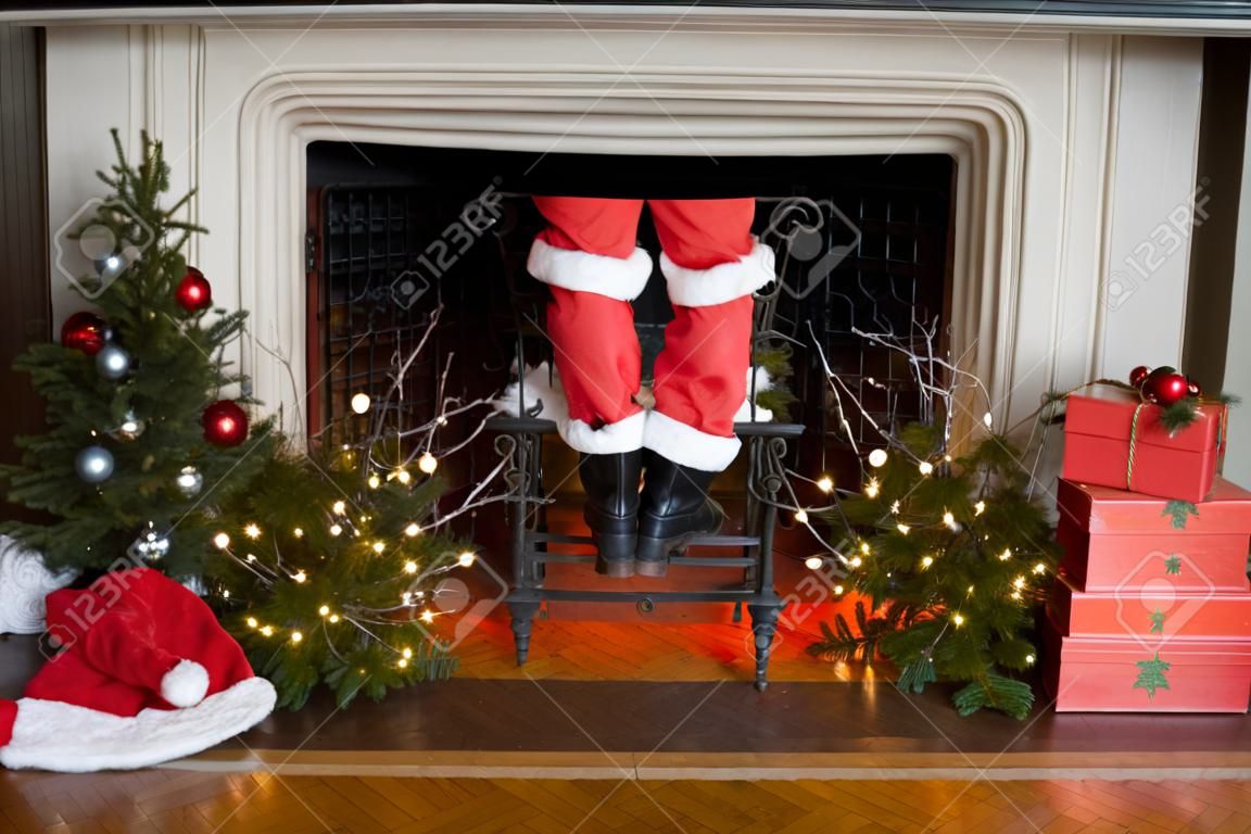 Babbo pantaloni e stivali venuta giù il camino con decorazioni di Natale intorno