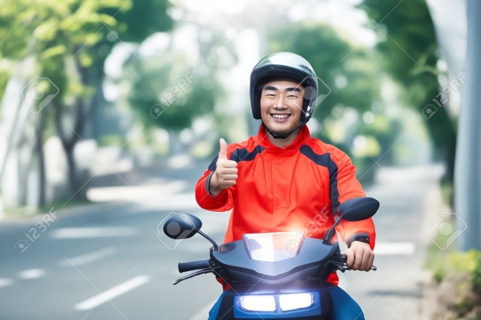 카메라에 엄지 손가락을 보여주는 상업 오토바이 드라이버로 행복 한 아시아 사람이 작동의 초상화