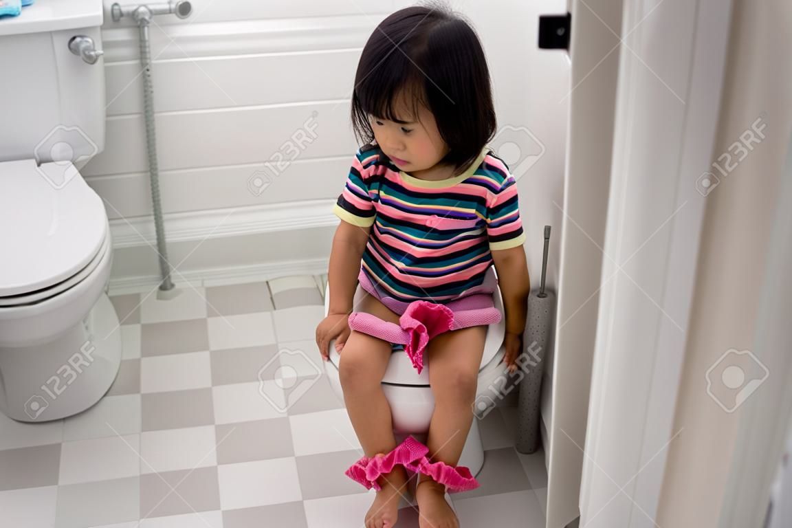 asian toddler sitting on toilet with pants down