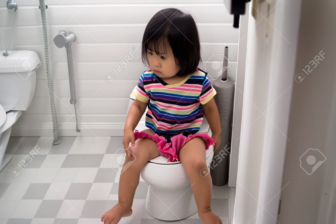 asian toddler sitting on toilet with pants down