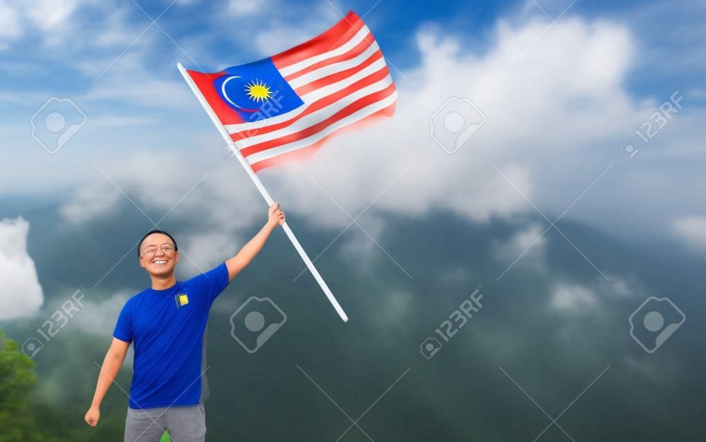 언덕 꼭대기에 자랑스럽게 서 있는 말레이시아 국기를 가진 아시아 남자