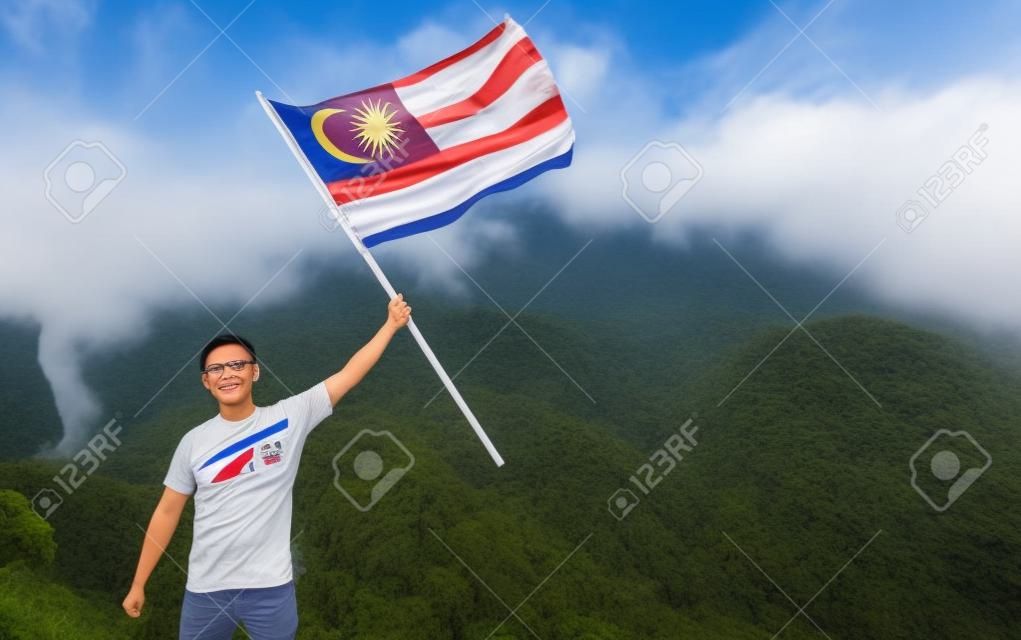 언덕 꼭대기에 자랑스럽게 서 있는 말레이시아 국기를 가진 아시아 남자