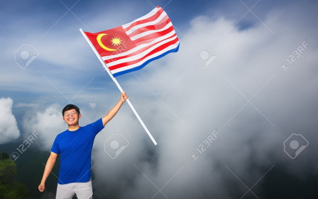 asian man with malaysia flag standing proudly on top of hill