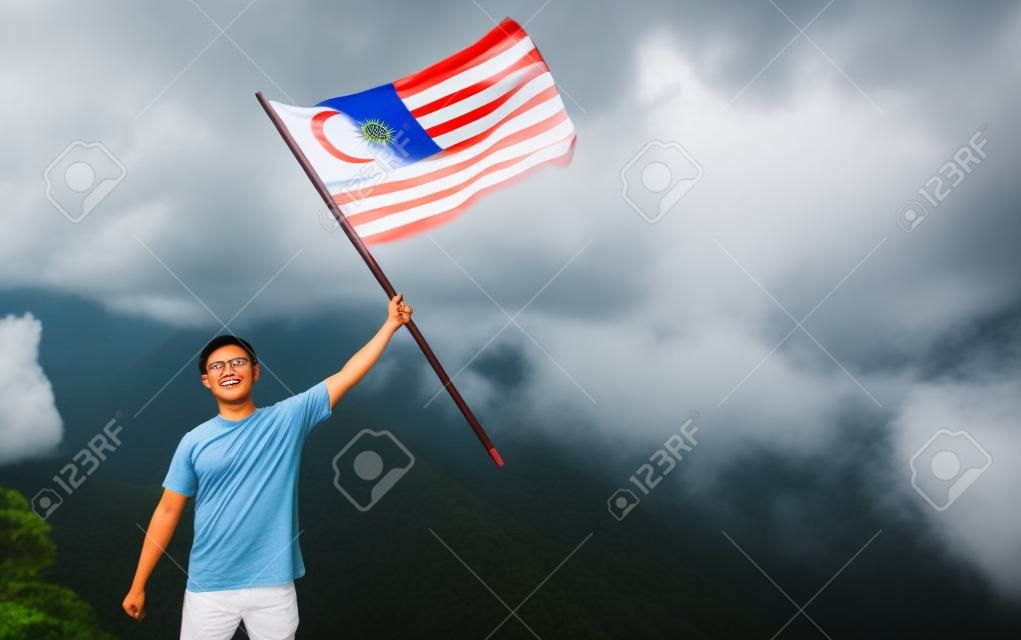 asian man with malaysia flag standing proudly on top of hill