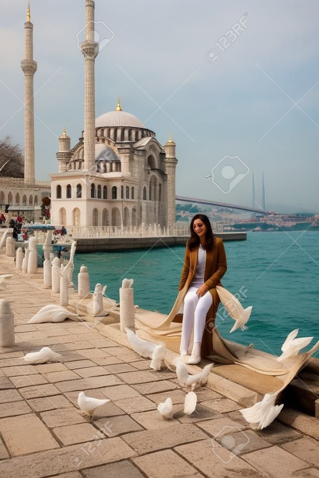 Schöne Frau sitzt in der Nähe des Bosporus mit der Ortaköy-Moschee im Hintergrund