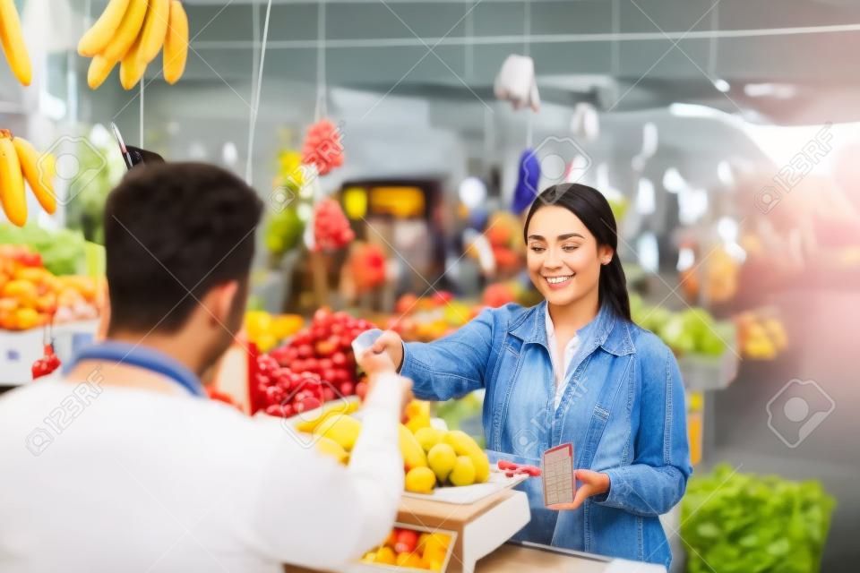 female customer giving her credit card to the seller for paying her fruits at cashier
