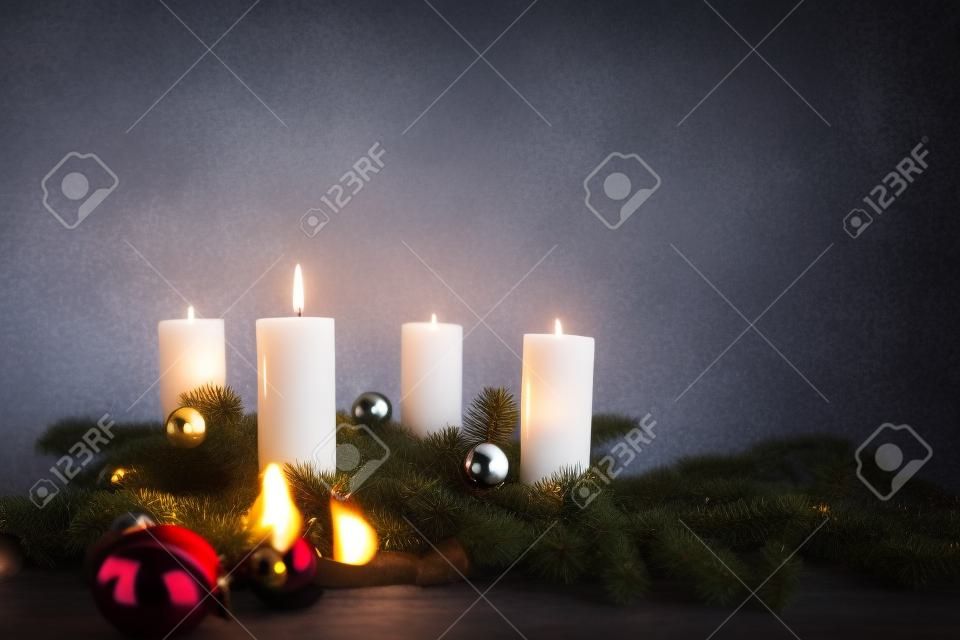 Jedna z czterech świec pali się na pierwsze przyjście na gałęzie jodły z dekoracją świąteczną na szarym tle, kopia przestrzeń, wybrane skupienie, wąska głębia ostrości