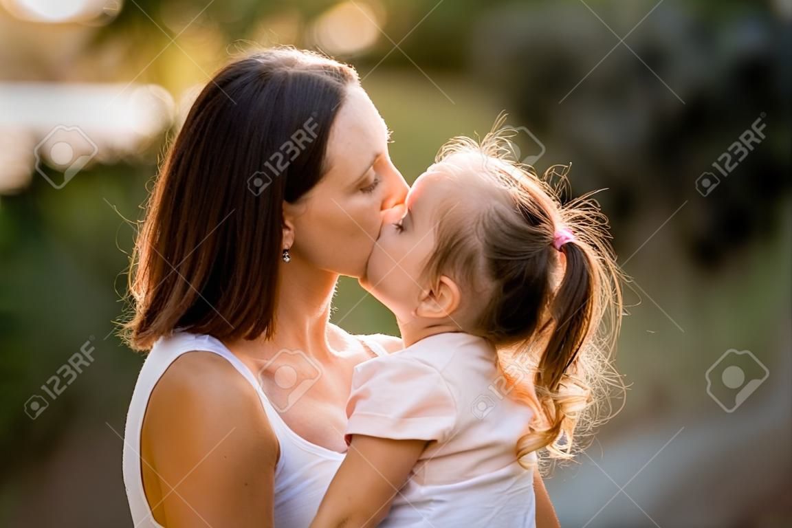 Primer plano de mujer con niña en sus brazos que se están besando.