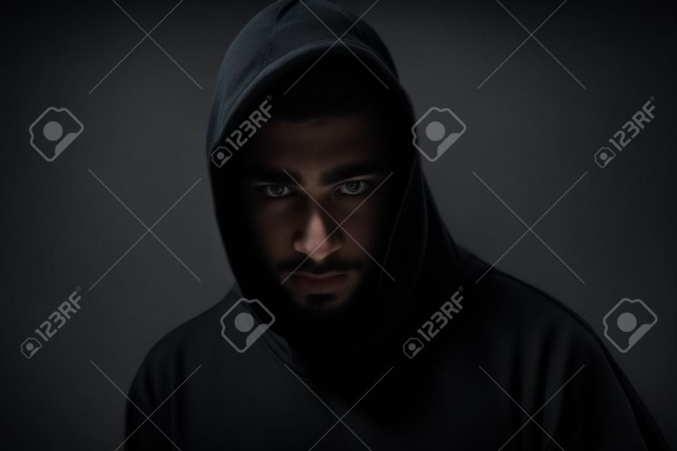 Hombre joven en negro sudadera con capucha invisible en la oscuridad de la noche, una luz tenue, los conceptos de peligro, el crimen, el terror