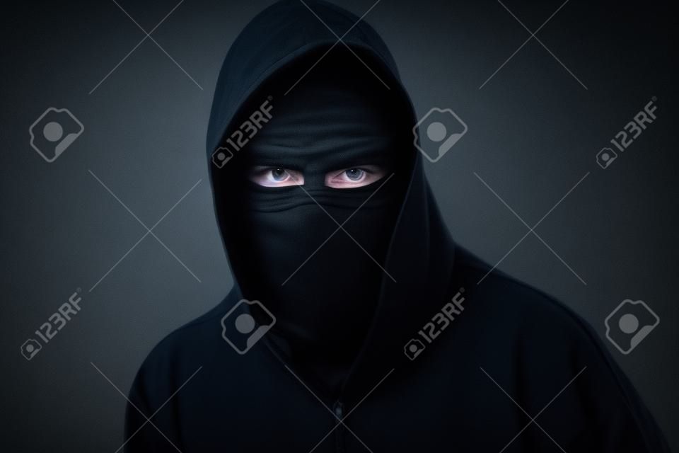 Fiatal férfi fekete kapucnis pulóver láthatatlan az éjszakai sötétségben, félhomályos, fogalmak a veszély, bűnözés, terror