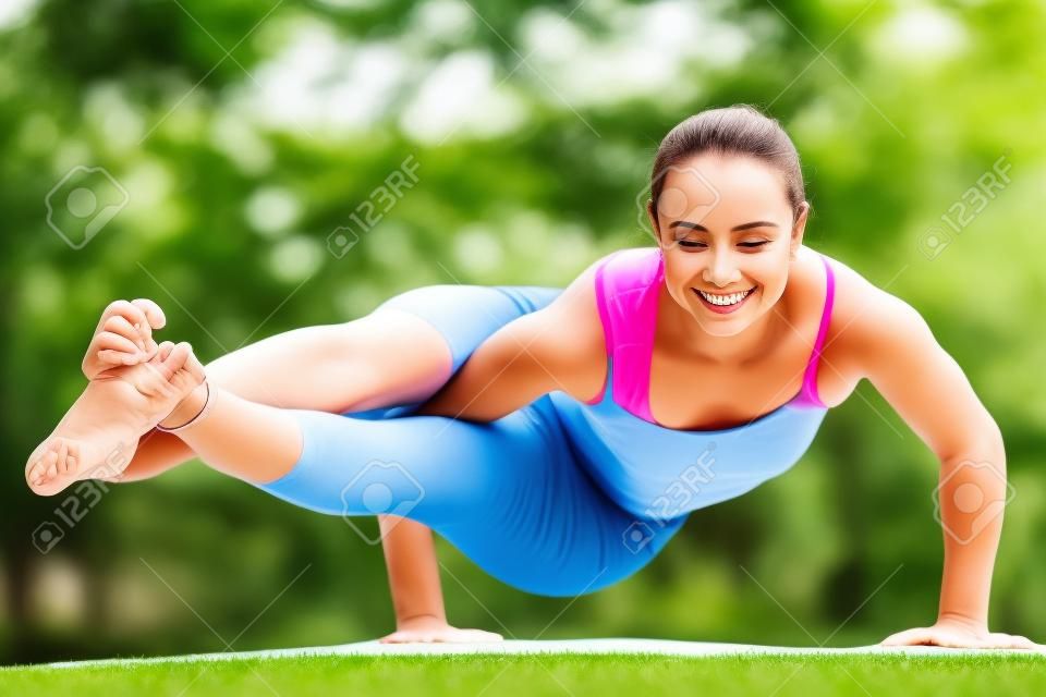 Gelukkige glimlach fit jonge mooie vrouw oefenen yoga buiten in het park op de zomerdag, het doen van asymmetrische arm balanceren oefening, asana Astavakrasana, achthoekige houding, volledige lengte