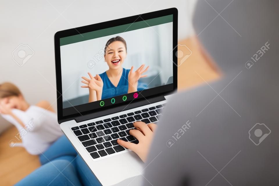 Two young women enjoy video call, communicating online with app for virtual chat, girlfriends talking online by laptop webcam, calling friend, stay in touch despite long distance, close up rear view
