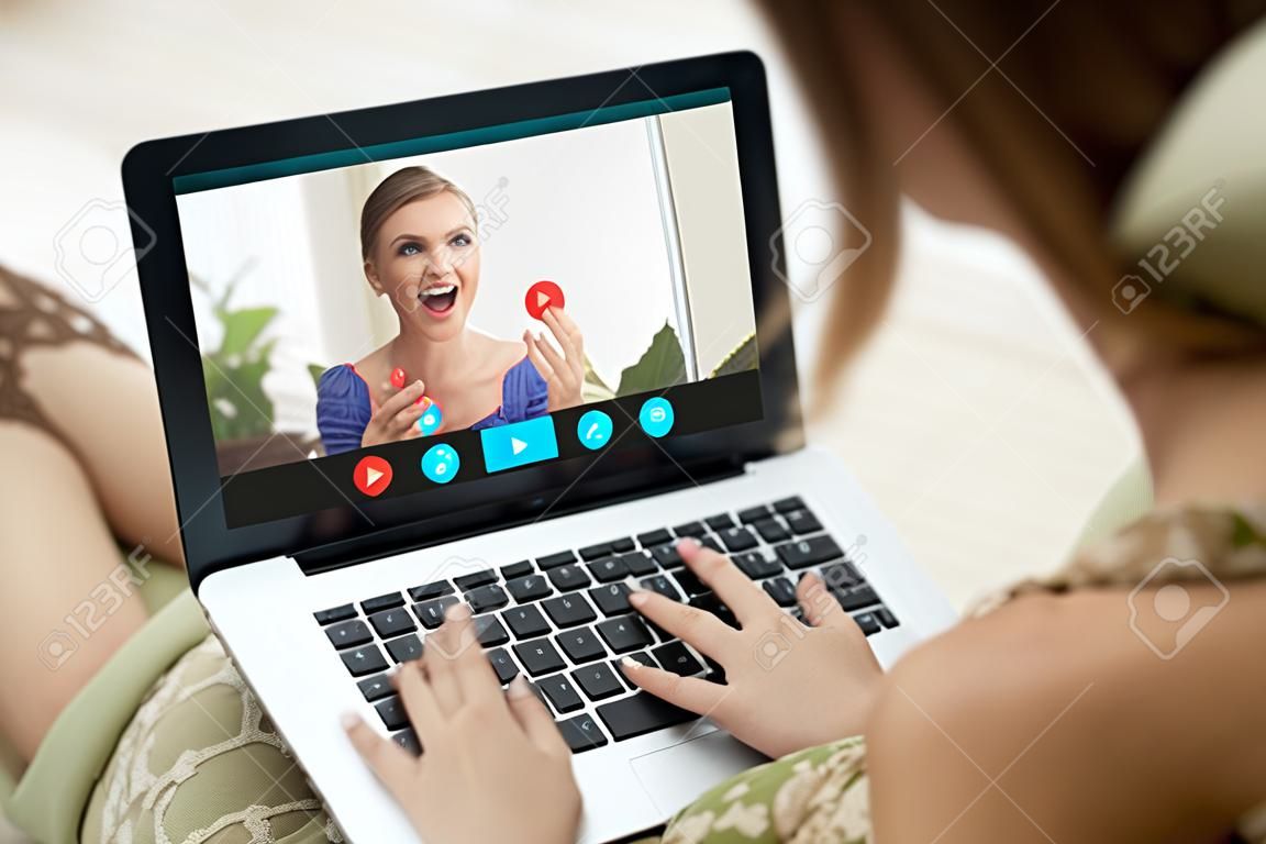 Two young women enjoy video call, communicating online with app for virtual chat, girlfriends talking online by laptop webcam, calling friend, stay in touch despite long distance, close up rear view