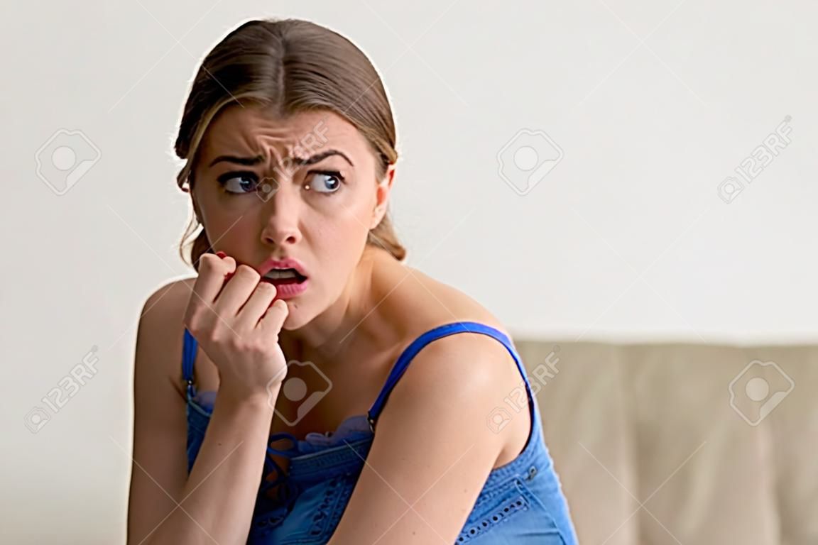 Headshot portrait of worried young woman biting nails and looking aside with fear. Frightened lady thinking about problems, afraid of difficulties, nervous because of bad relationship with boyfriend