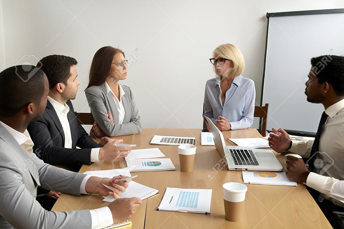 Komoly idős üzletasszony vezető vállalati csoporttalálkozó, többnemzetiségű alkalmazottakkal beszélget, vezető női főnök vezérigazgató, különféle beosztottakkal folytatott munka megbeszélése a vállalatcsoport tájékoztatóján