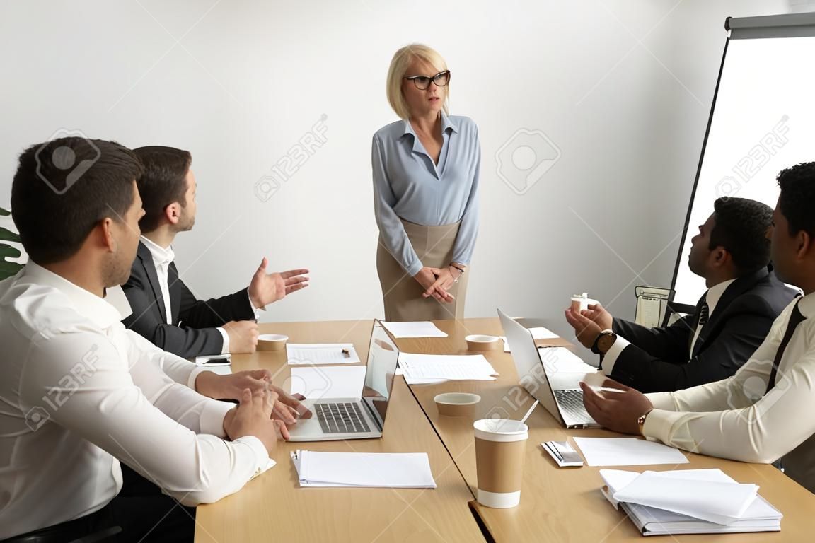 严重的老年的女商人领导公司团队会议与多种族雇员交谈，高级女老板首席执行官领导在公司集团简报会上与下属讨论工作