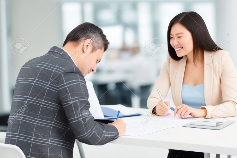 Caucasian businessman signing contract buying business insurance or taking loan at meeting with asian hr businesswoman