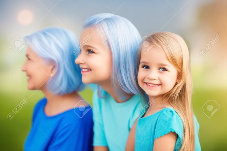 Portrait of cute little girl looking at camera smiling, mother and grandmother watch in distance imagining bright future for family, three generations of women in one picture, profile shot