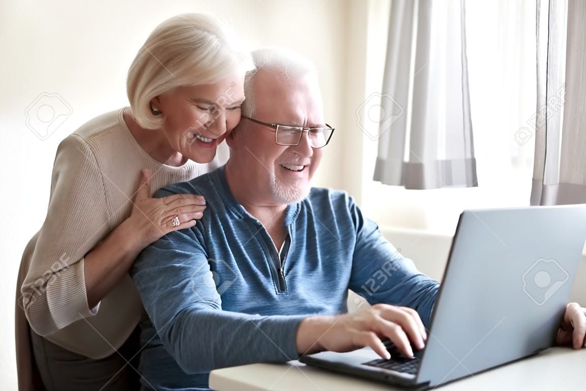 Un mari âgé excité utilisant un ordinateur portable montrant une femme souriante quelque chose à l'écran, un couple de personnes âgées heureux regardant un ordinateur, regardant des photos ensemble ou une vidéo amusante en ligne. Concept de personnes âgées et de technologie