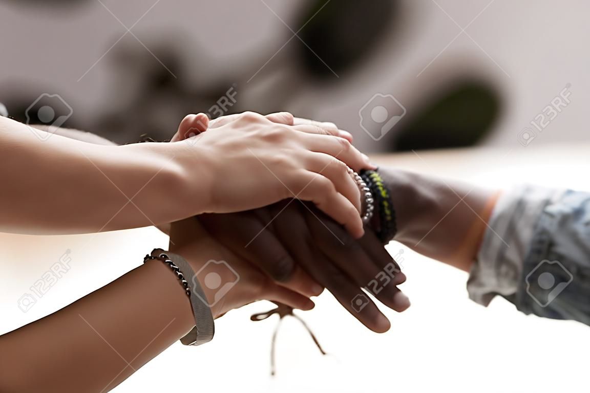 Close up diverse male female sitting holding hands together. Multiracial people starting common business or celebrate success at work stacked hands together showing unity support, all for one concept