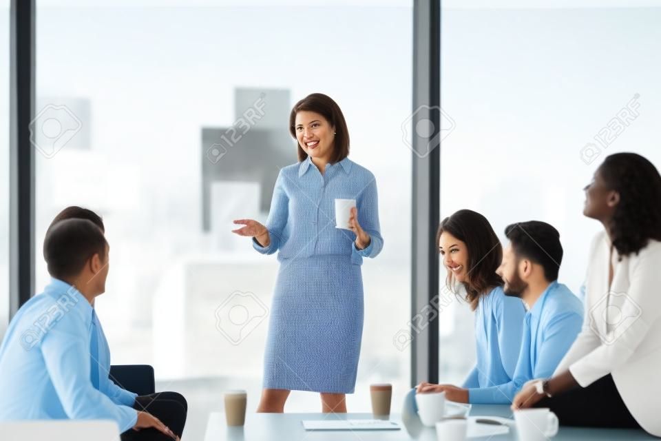Happy mature ceo coach mentor leader talking to diverse team employees chatting at business meeting, friendly office workers group and middle aged female boss have fun conversation at coffee break