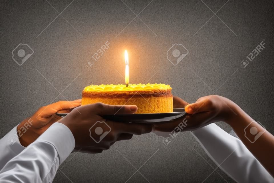 Nahaufnahme des Arbeiters gratuliert Kollegen zum Geburtstag, präsentiert gebackenen Kuchen mit brennender Kerze, Mitarbeiter grüßt Mitarbeiter, gibt Sahnetorte, feiert, schmeißt eine Party im Büro