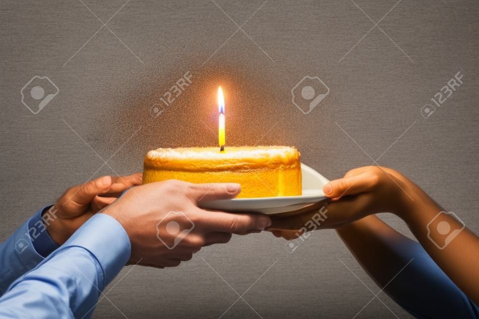 Nahaufnahme des Arbeiters gratuliert Kollegen zum Geburtstag, präsentiert gebackenen Kuchen mit brennender Kerze, Mitarbeiter grüßt Mitarbeiter, gibt Sahnetorte, feiert, schmeißt eine Party im Büro