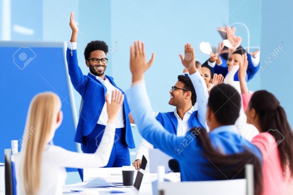Diverse business people group raise hands at corporate presentation training, happy multi-ethnic employees team participate in vote volunteering, ask questions at conference with african coach leader
