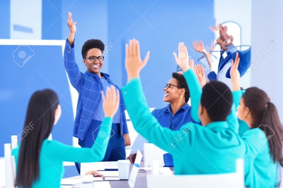 Diverse business people group raise hands at corporate presentation training, happy multi-ethnic employees team participate in vote volunteering, ask questions at conference with african coach leader