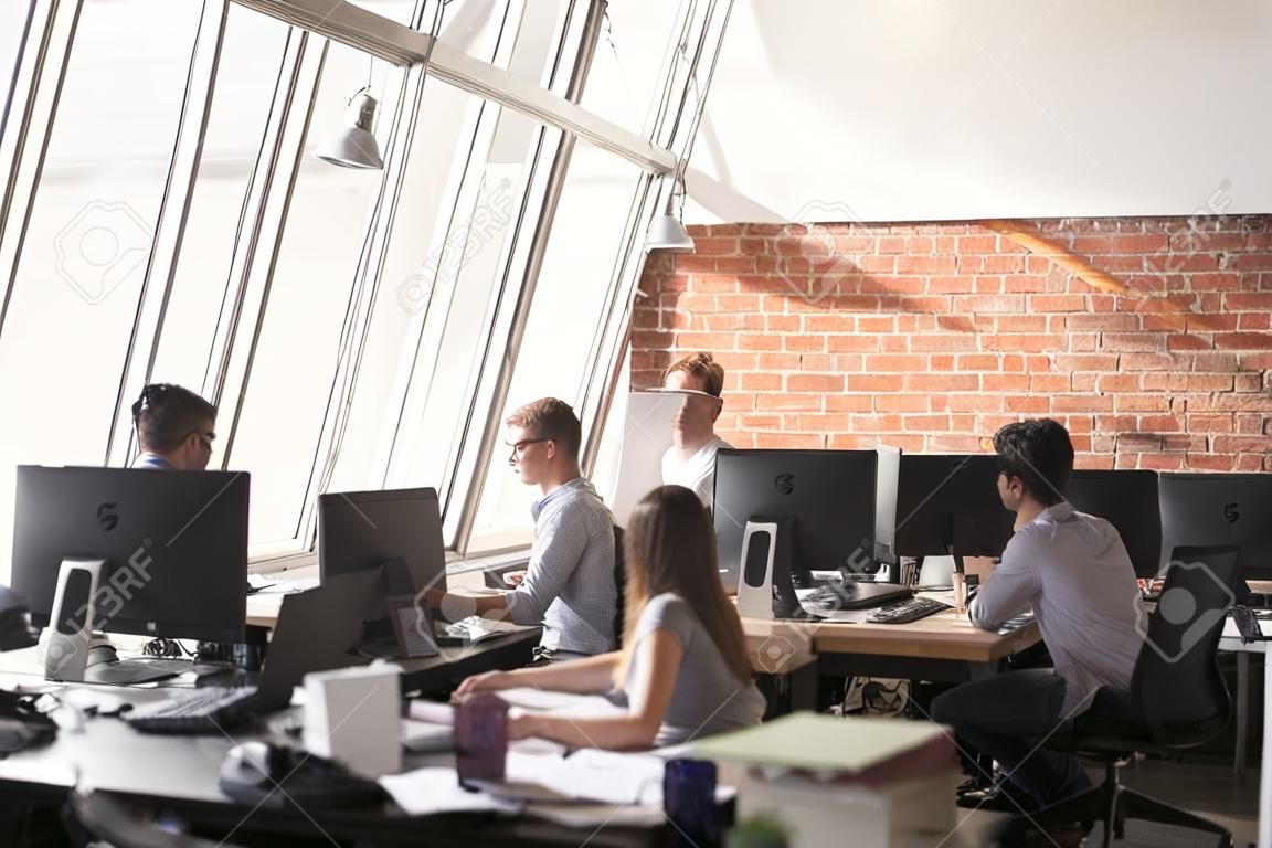 Werknemers mannelijke vrouw die in coworking open ruimte met drukke werkdag met behulp van computers zitten aan de balie, achteraanzicht.