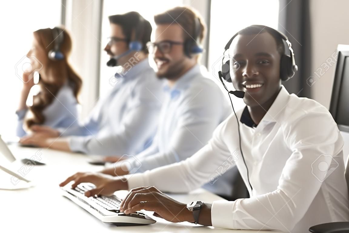 Szczęśliwy afrykański biznesmen agent call center w zestawie słuchawkowym patrzący w kamerę w miejscu pracy, uśmiechnięty czarny mężczyzna operator telemarketera pracuje na komputerze w biurze pomocy technicznej obsługi klienta, portret