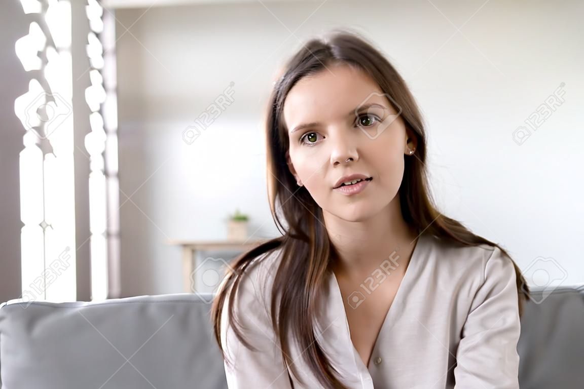 Head shot portrait young woman sitting on couch looking at camera having conversation using computer webcam modern tech talking with friend, girl recording vlog passing job interview distantly concept