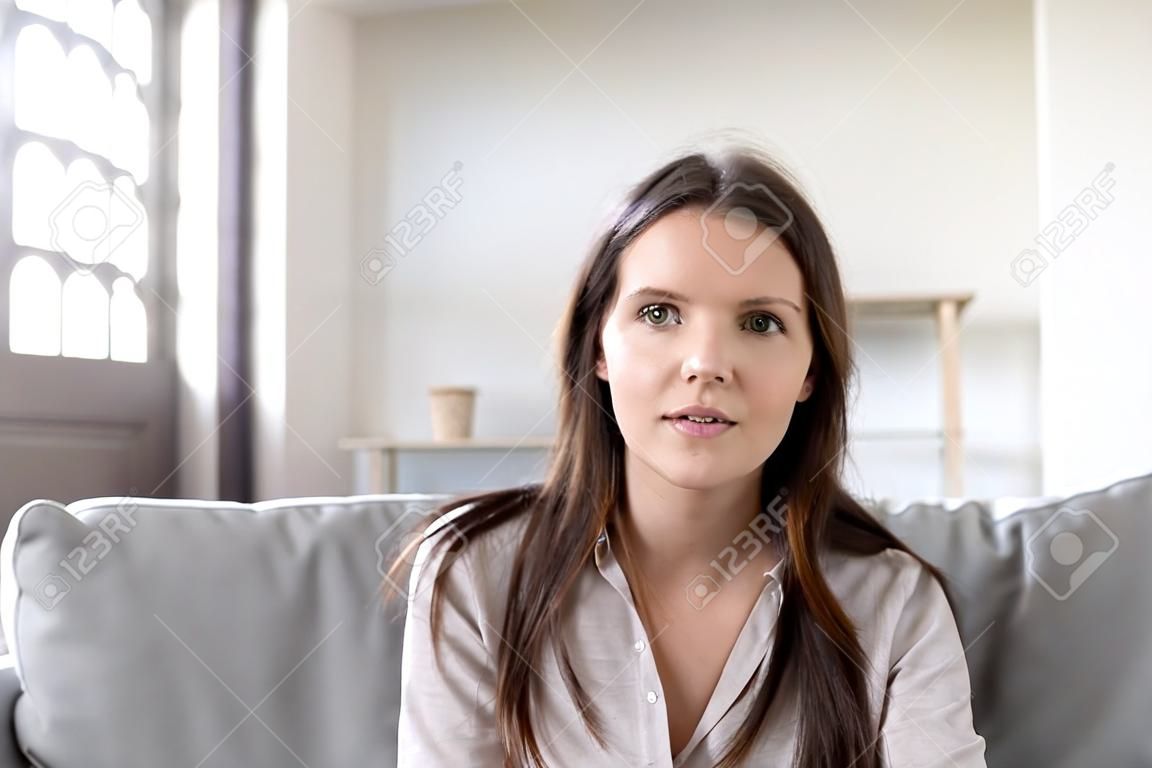 Head shot portrait young woman sitting on couch looking at camera having conversation using computer webcam modern tech talking with friend, girl recording vlog passing job interview distantly concept