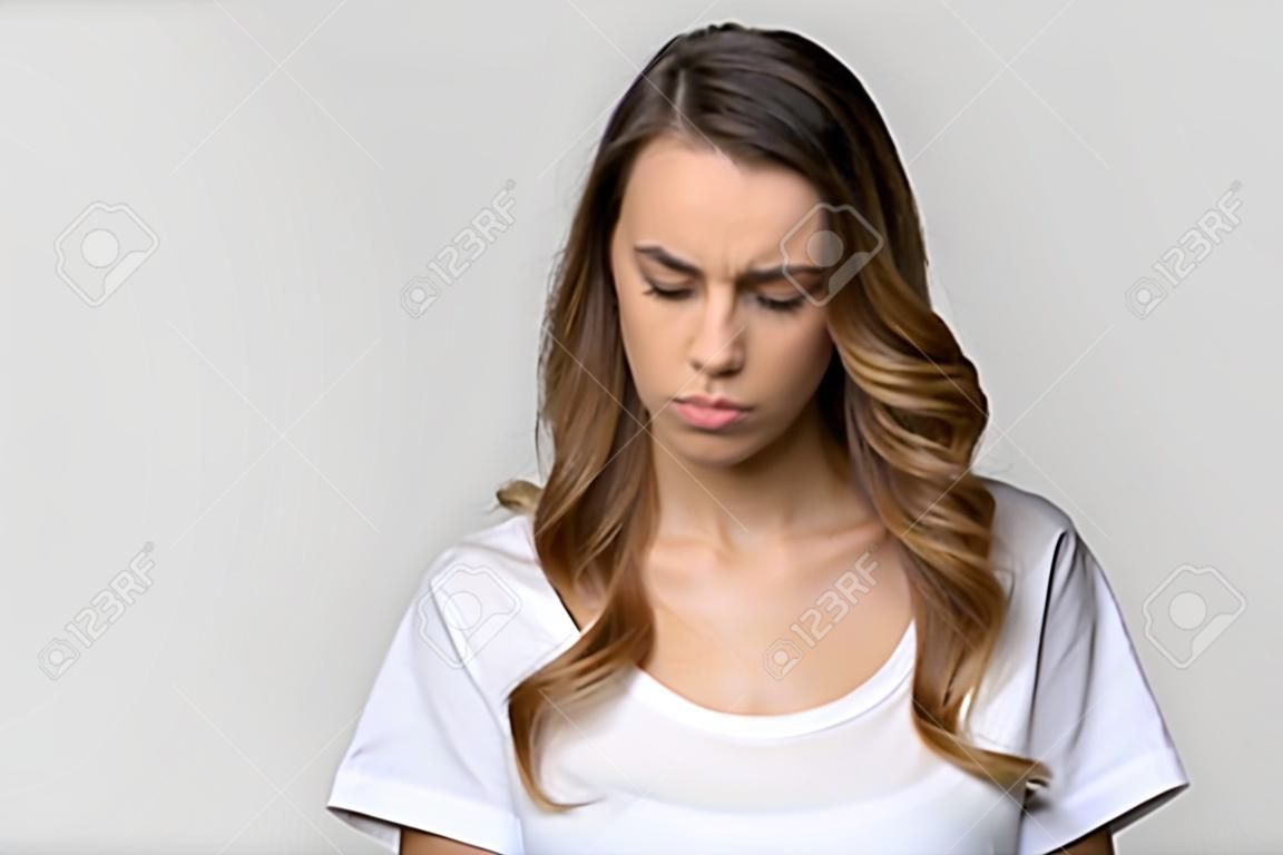 Head shot studio portrait millennial attractive woman on grey background feels badly, negative emotions facial expression concept of frustration sadness disappointment having problem and difficulties