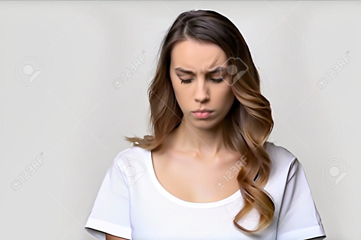 Head shot studio portrait millennial attractive woman on grey background feels badly, negative emotions facial expression concept of frustration sadness disappointment having problem and difficulties