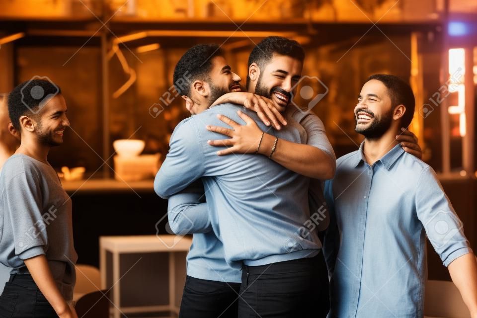 Different ethnicity multi racial guys hugging greeting each other best friends gathered in public place, spending Friday hanging out together, chance meeting, friendship between diverse people concept