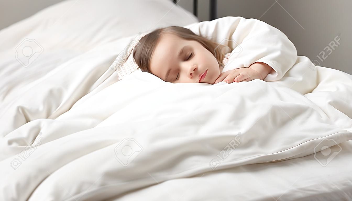 落ち着いた愛らしい小さな娘は一日昼寝をします。寝室のベッドの快適なマットレスに横たわっている白い新鮮な羽毛布団で覆われた静かな就学前の女の子。健康な十分な睡眠、zzz、おやすみ、コンセプト