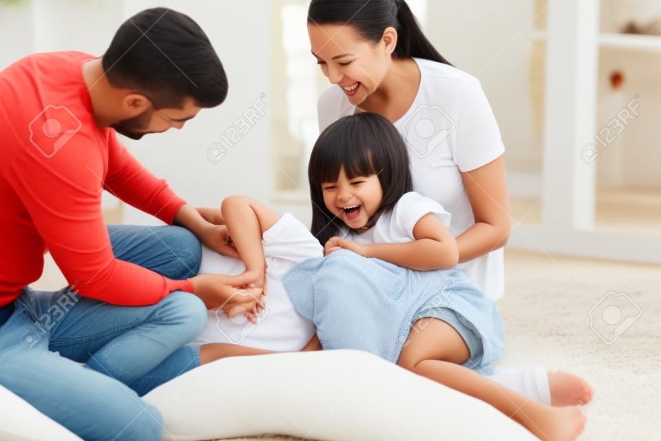 Happy family mom dad and little cute children son daughter laughing tickling on floor, parents couple having fun with small funny kids playing cuddling together at home enjoy lifestyle activity