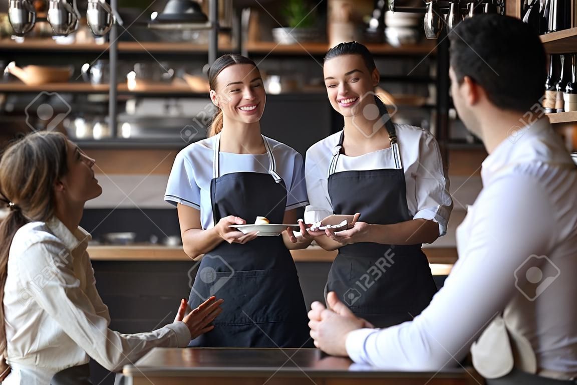 Uśmiechnięta kelnerka nosi fartuch trzymaj notatnik długopis zamawiaj porozmawiaj z klientami obsługującymi gości restauracji para wybierając jedzenie napoje menu usiądź w kawiarni stolik kawowy, kelnerzy, dobra obsługa klienta
