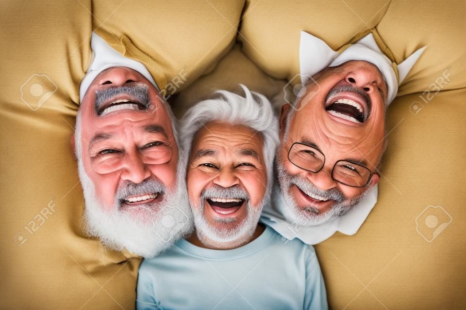 Happy multi 3 three generation family lying in row looking at camera, smiling child boy son grandson, young adult father and old senior grandfather laughing bonding, close up portrait, above top view