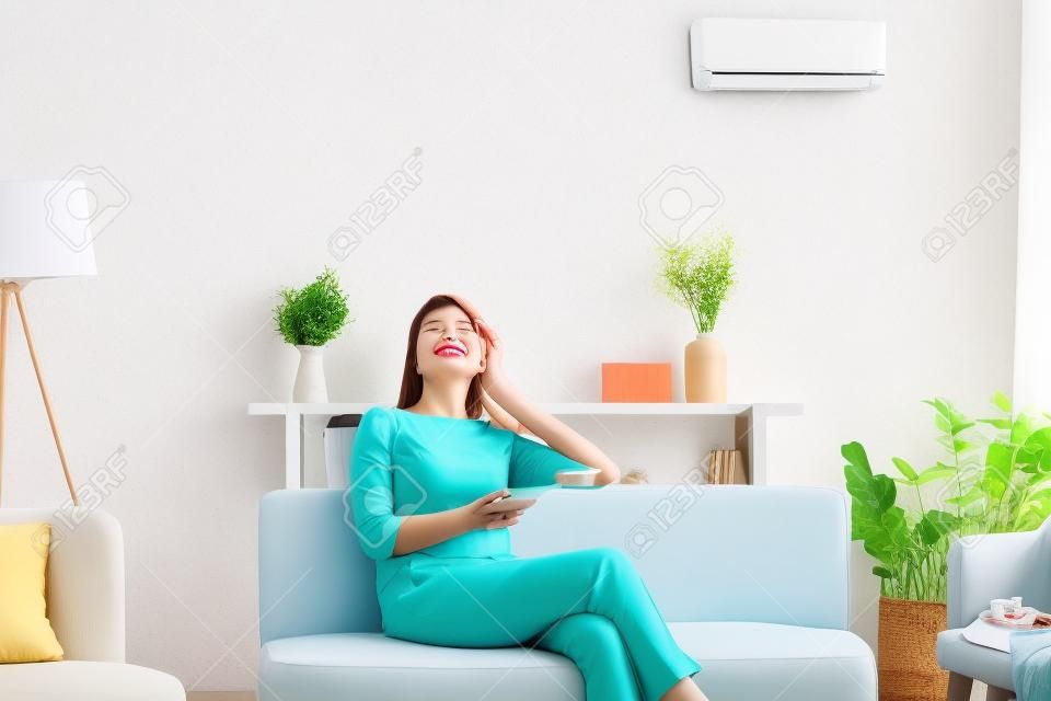 Une femme des années 50 se repose sur un canapé les yeux fermés profite de l'air frais tient la télécommande utilise le climatiseur se refroidit par une chaude journée d'été en ajustant la température à l'intérieur du salon, le concept de vie de bien-être
