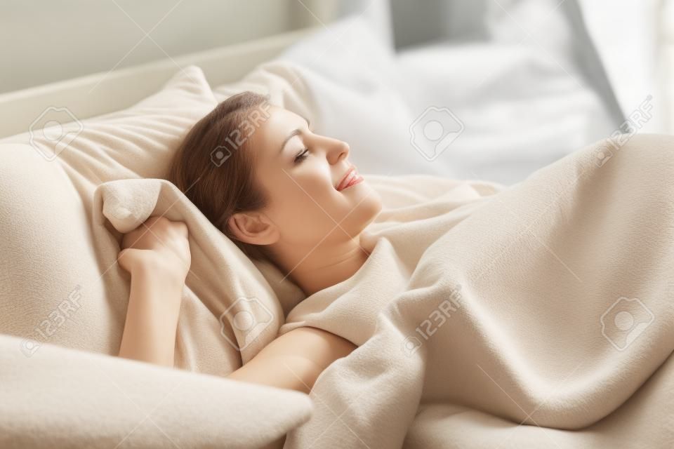 Middle-aged attractive woman lying in bed on comfortable memory foam pillow fresh beige color bed clothes enjoying early morning awakened at home closed eyes dreaming visualizing perfect day concept