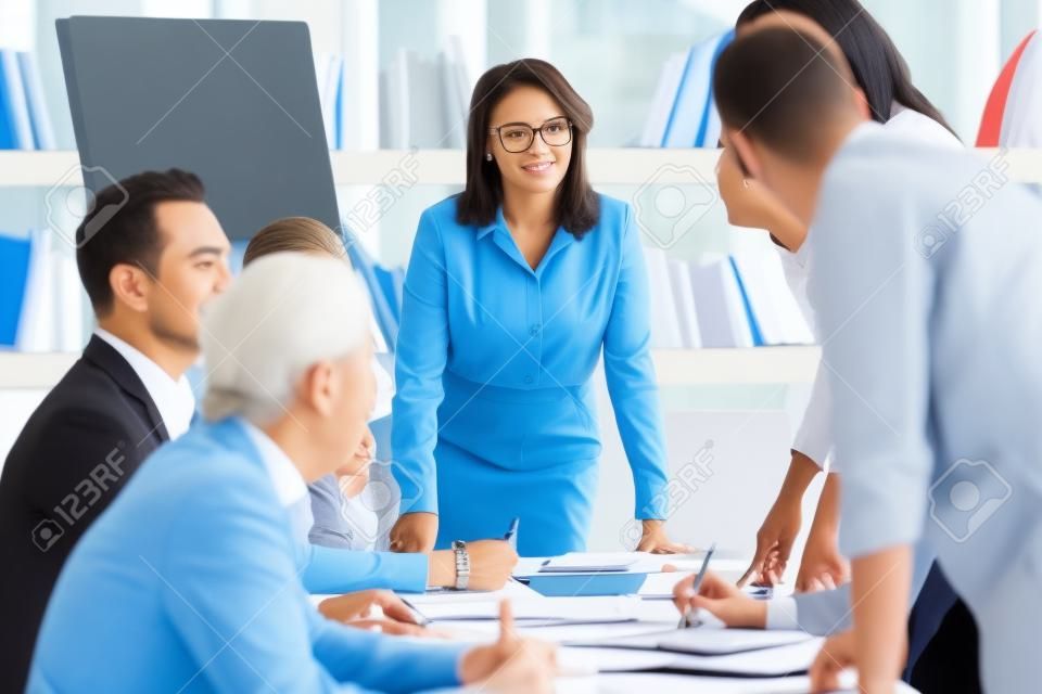 Multi-ethnic team members takes part in briefing lead by aged businesswoman company boss, businesspeople feels satisfied succeed agreement acceptable to both parties, mentoring or negotiations concept