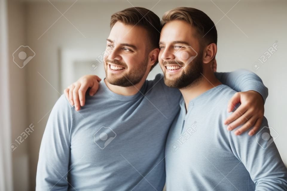 Head shot excited grown up son embracing shoulders of happy middle aged father, looking at window. Positive two male generations family supporting each other, visualizing planning future together.
