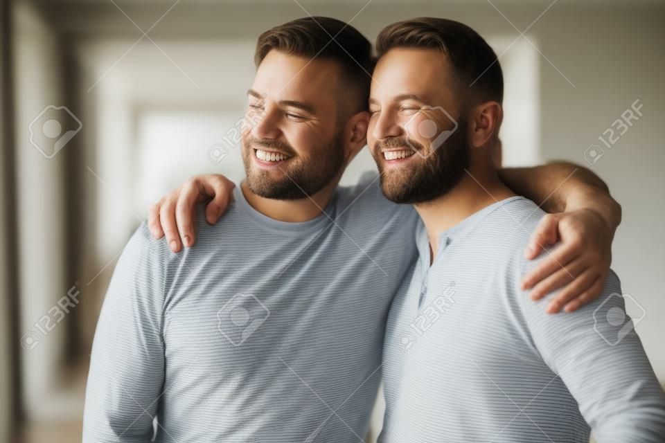 Head shot excited grown up son embracing shoulders of happy middle aged father, looking at window. Positive two male generations family supporting each other, visualizing planning future together.