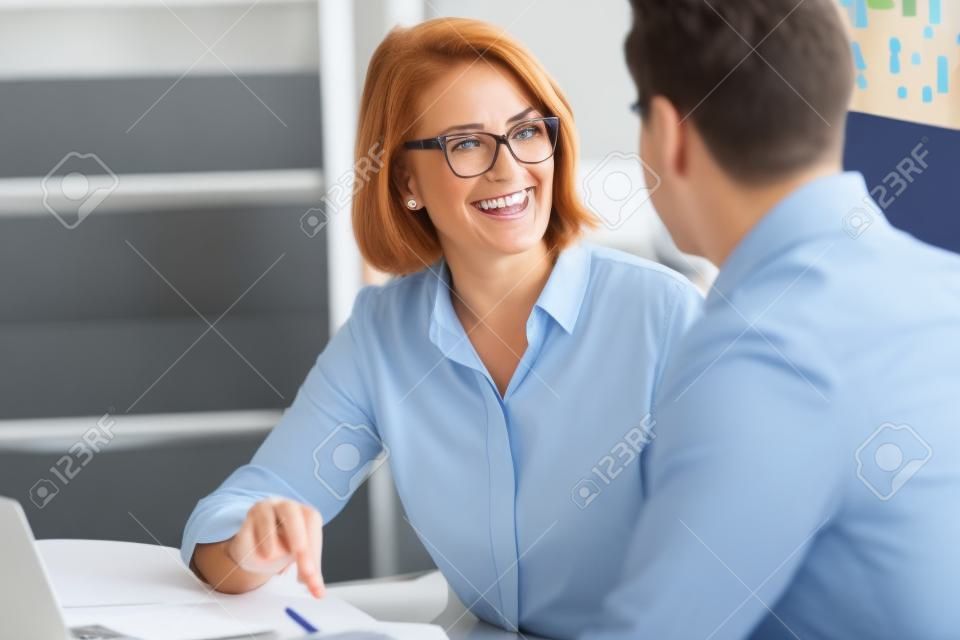Sorrindo de meia-idade do sexo feminino empregado falar brainstorm com o colega do sexo masculino no escritório briefing na sala de reuniões, feliz diversos colegas de trabalho se divertir rir cooperar discutir idéias na reunião
