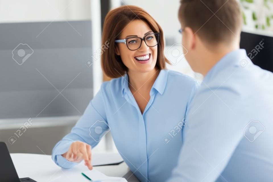 Sorrindo de meia-idade do sexo feminino empregado falar brainstorm com o colega do sexo masculino no escritório briefing na sala de reuniões, feliz diversos colegas de trabalho se divertir rir cooperar discutir idéias na reunião