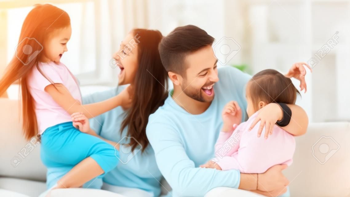 Padres emocionados divirtiéndose con dos hijas pequeñas en casa, lindas niñas preescolares con una madre y un padre amorosos y felices sentados en el sofá en casa, abrazándose y riéndose, la familia pasando el fin de semana juntos