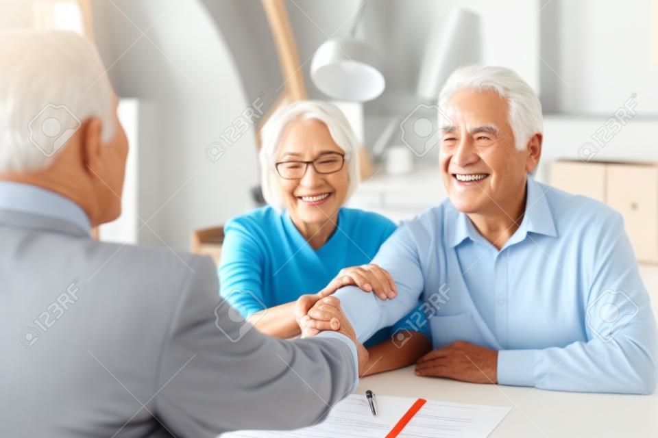 Happy grateful elderly couple of clients thanking real estate agent, lawyer, broker for help with house buying or selling, medical treatment contract, insurance agreement signing, giving handshake