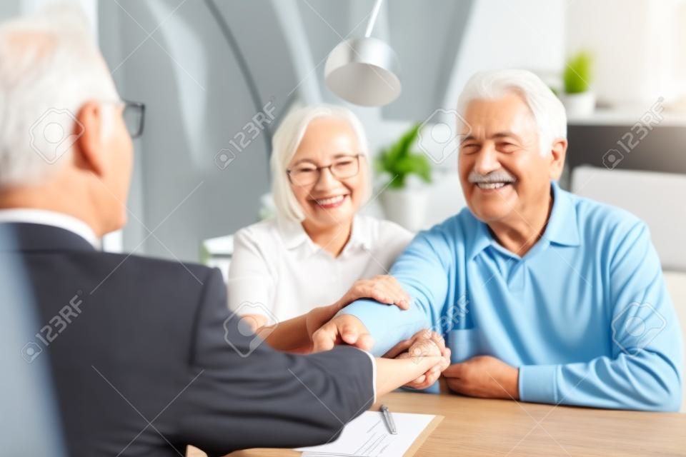 Happy grateful elderly couple of clients thanking real estate agent, lawyer, broker for help with house buying or selling, medical treatment contract, insurance agreement signing, giving handshake